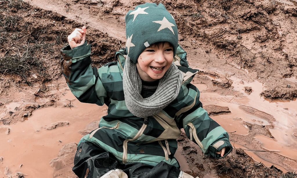 Ein Junge sitzt glücklich in einer Matsch-Pfütze