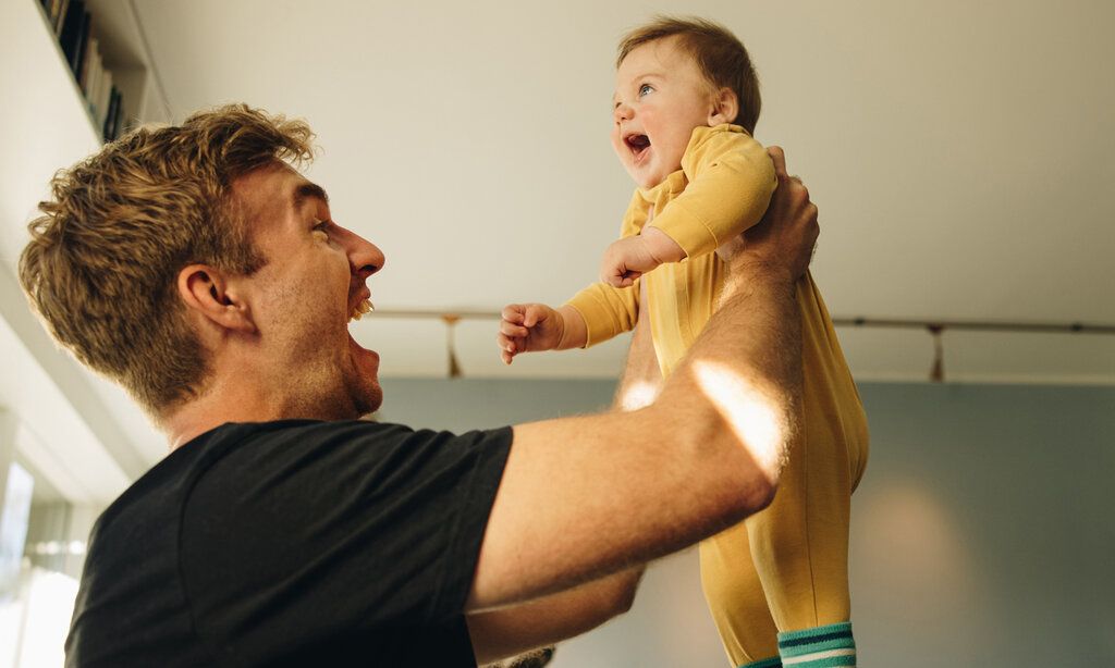 Vater hält Baby hoch und lacht
