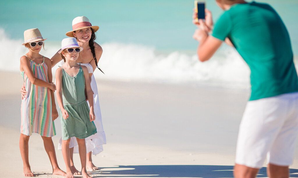 Vater fotografiert seine Frau und zwei Töchter am Strand, im Hintergrund Brandung