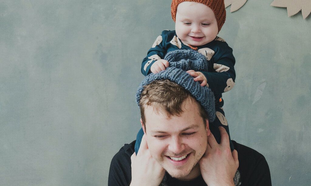 Junger Vater trägt Baby auf Schultern, Baby zieht Vater die Mütze aus