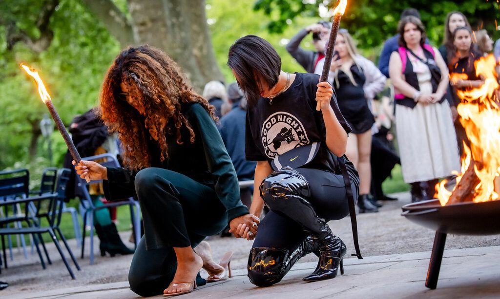 Zwei Frauen mit fackeln knien zusammen, im Hintergrund Publikum
