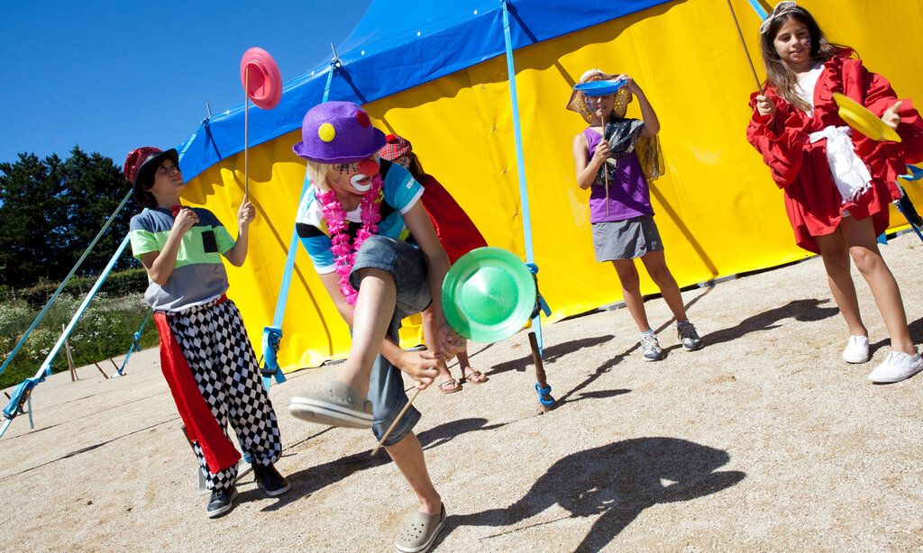 Verkleidete Kinder jonglieren mit Diabolos vor einem Zirkuszelt