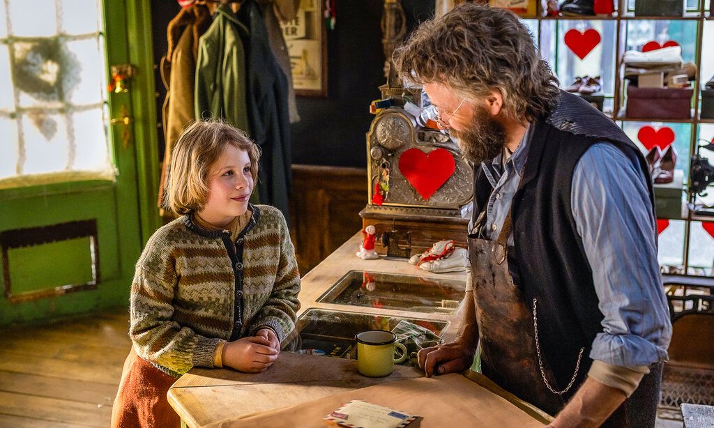 ein Kind steht bei einem Schuster am Verkaufstresen und spricht mit ihm