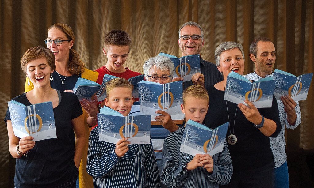Neun Leute stehen zusammen und singen, in den Händen halten sie das Weihnachtsliederheft