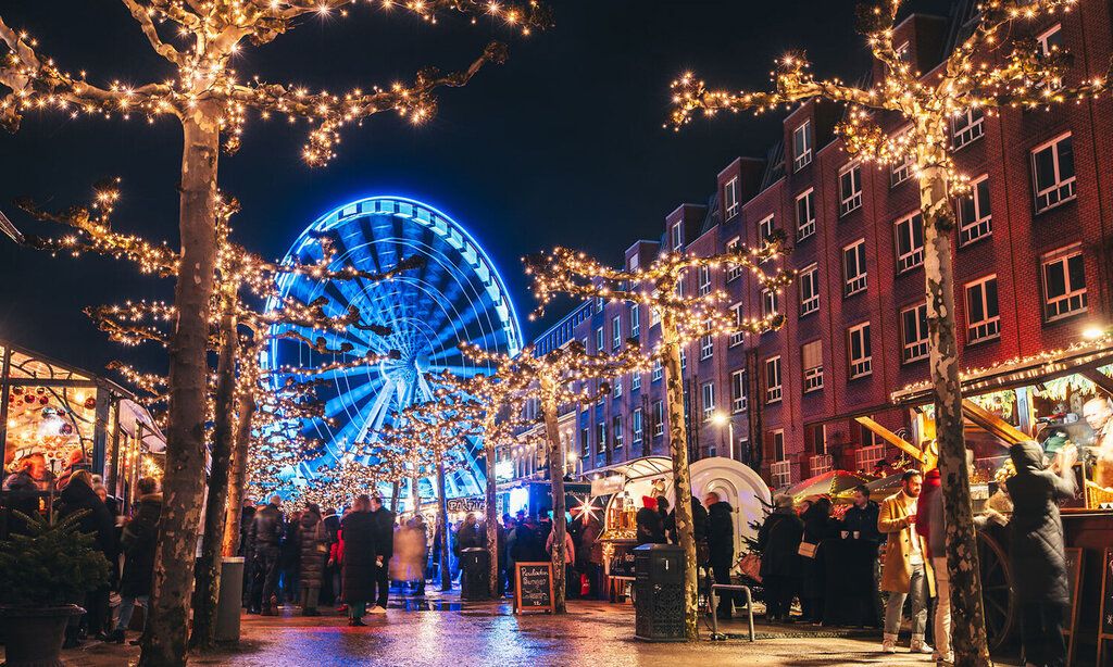 Weihnachtsmarkt-Stände auf der Rheinuferpromenade Düsseldorf am Abend, im Hintergrund das beleuchtete Riesenrad