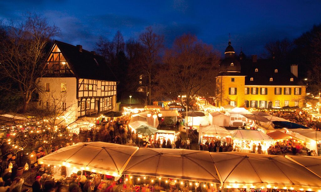 Weihnachtsmarkt Schloss Lüntenbeck am Abend, Verkaufsstände vor Fachwerkhaus und Schloss festlich beleuchtet