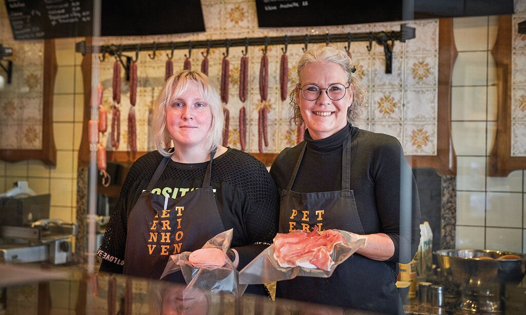 Zwei Verkäuferinnen stehen hinter der Ladentheke und präsentieren Wurst und Schinken