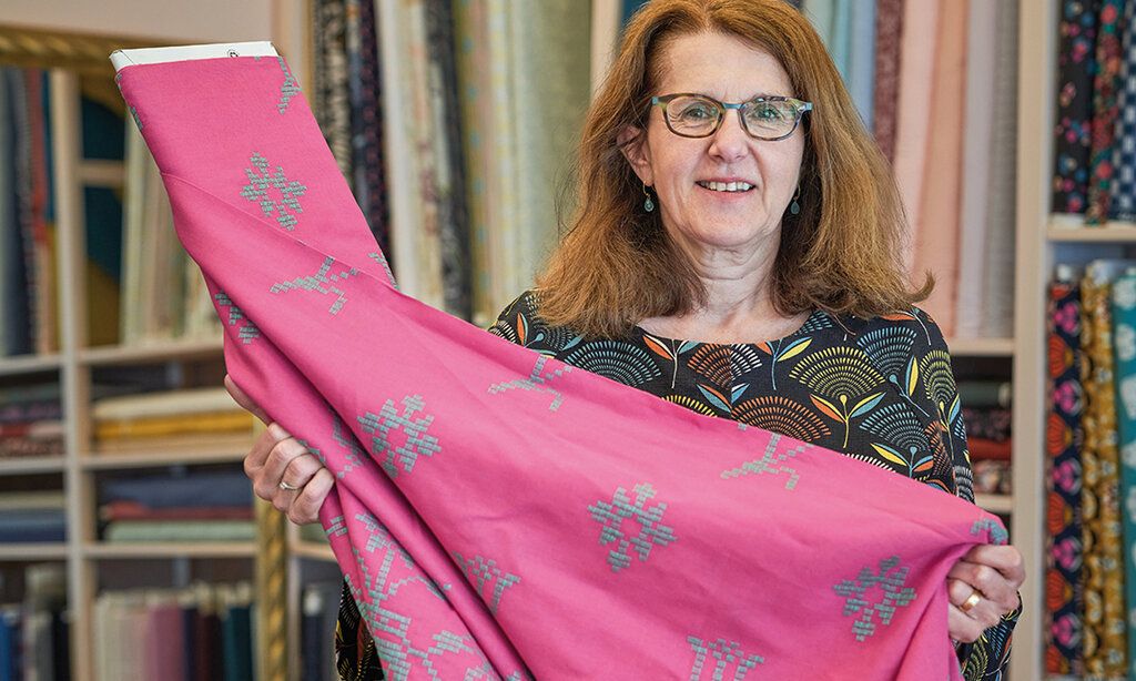 Inhaberin Sabine Kirsch hält eine Rolle pinken Stoff in der Hand und lächelt in die Kamera. Im Hintergund das Ladenlokal Stofffairliebt.