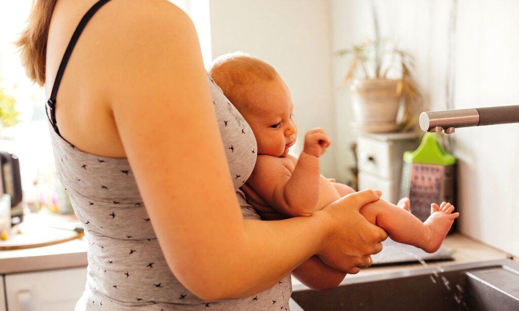 Eine Mutter hält ihr Baby über dem Waschbecken ab und das macht Pipi