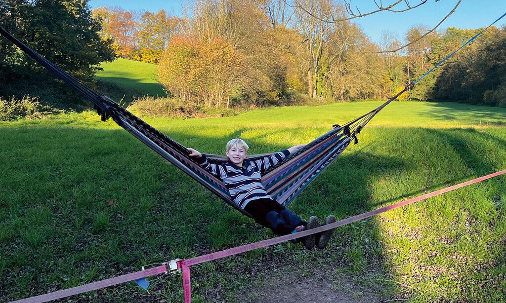 Junge auf Hängematte, im Hintergrund eine große Wiese mit Bäumen, herbstlich