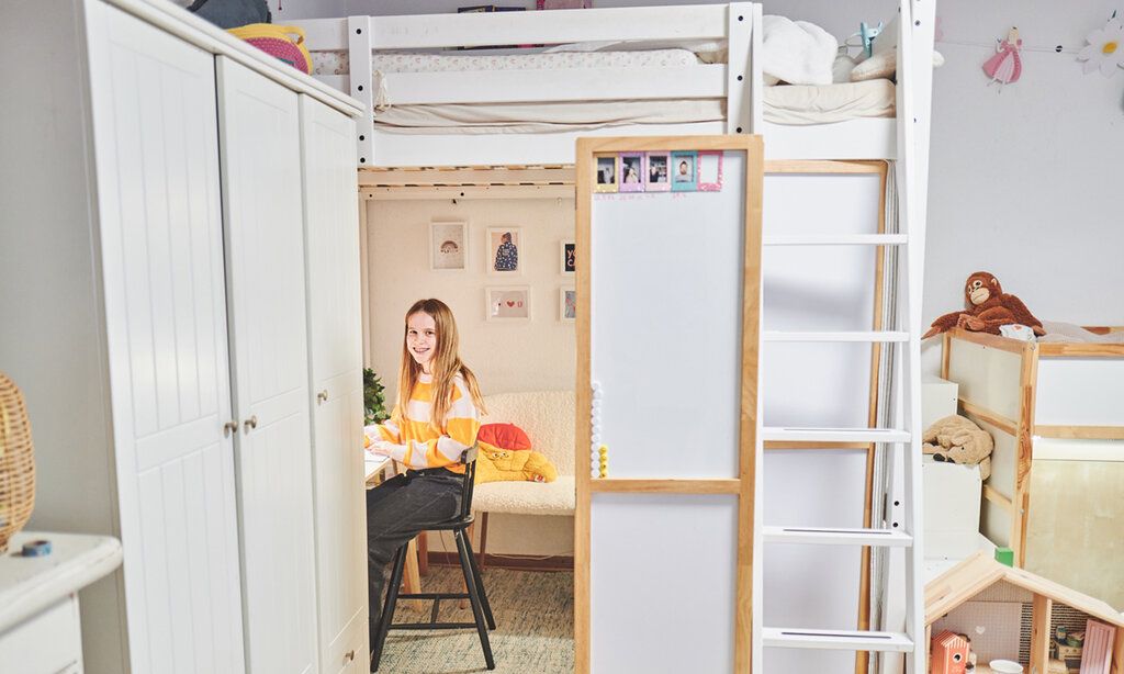 Kinderzimmer, Mädchen sitzt unter seinem Hochbett am Schreibtisch und lächelt in die Kamera
