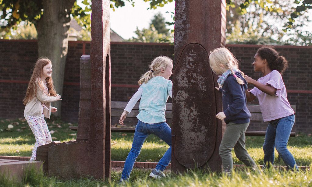 Vier Kinder haben Spaß während sie im freien um Stahlskulpturen laufen