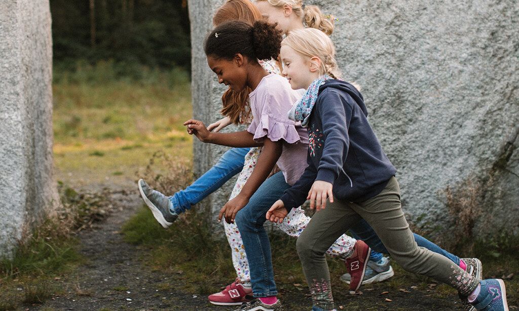 Vier Kinder spielen draussen vor Steinskulptur