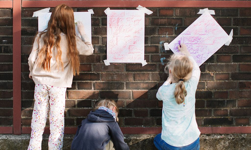 Drei Kinder malen auf Papier an einer Backsteinwand