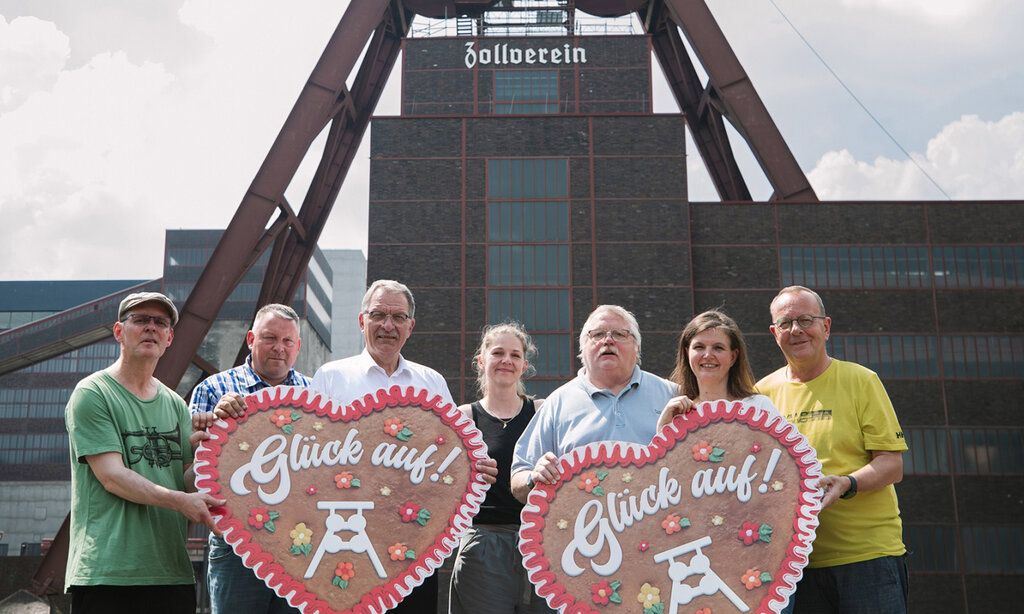 Sieben Leute stehen mit zwei großen Lebkuchenherzen vor der Zeche Zollverein