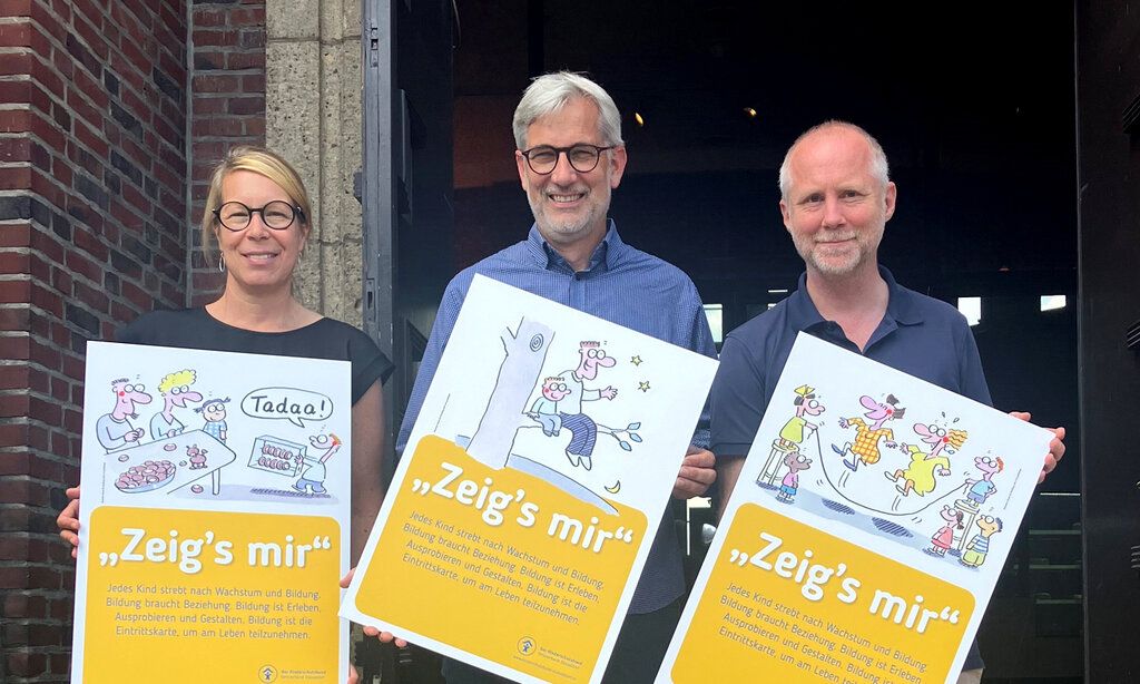 Eine Frau und zwei Männer stehen vor dem NRW Forum und zeigen Plakate des Kinderschutzbundes.