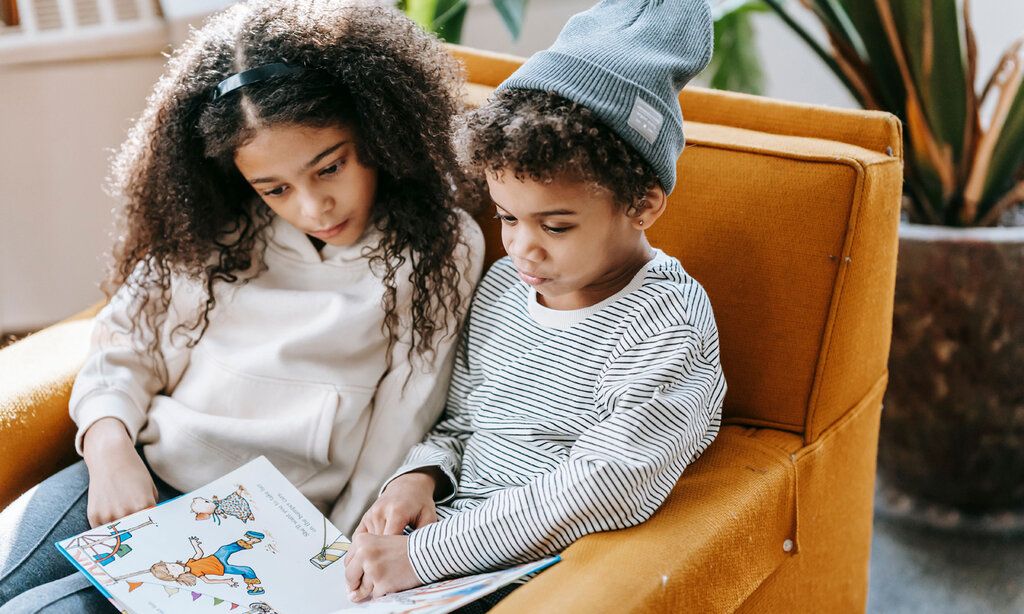 Zwei Kinder sitzen auf einem Sessel und lesen ein Buch
