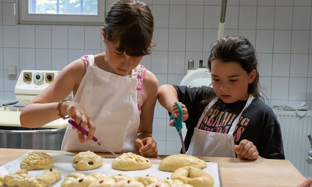 zwei Mädchen in der Backstube, vor ihnen liegen geformte, rohe Hefeteiggebilde