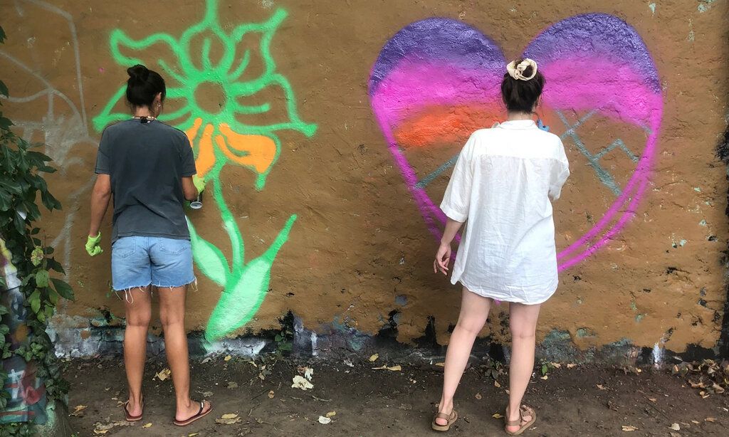 Zwei Mädchen sprühen Graffiti an eine Wand