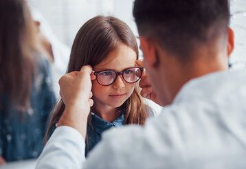 Optiker hilft jungem Mädchen mit Brille