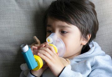 Kind auf Sofa mit Asthmaspray