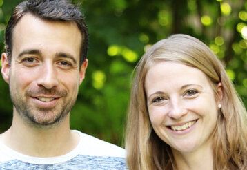 Philipp und Andrea Bettinger lächeln in die Kamera, im Hintergrund Gebüsch