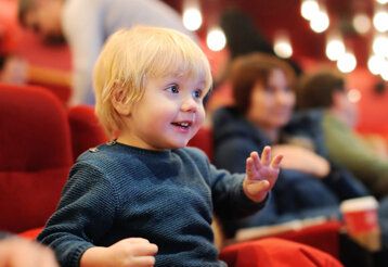 Kleiner Junge sitzt auf rotem Sessel im Theater und ist begeistert