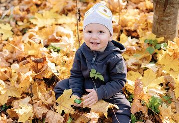 Lachendes Kleinkind mit Mütze sitzt im gelben Herbstlaub