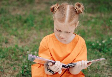 Ein Mädchen liest in einem Buch, im Hintergrund Wiese