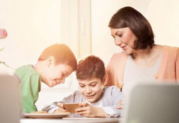 Zwei Söhne spielen mit dem Smartphone, Mutter schaut zu