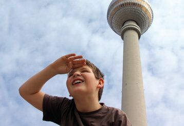 Junge steht vor Berliner Fernsehturm und guckt in die Ferne