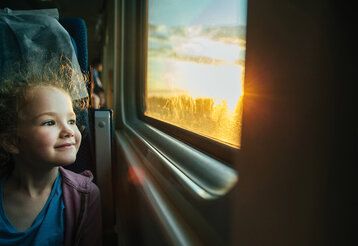 Mädchen sitzt im Zug und schaut aus dem Fenster