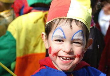 kleiner Junge als Clown verkleidet in einer Menschenmenge draußen