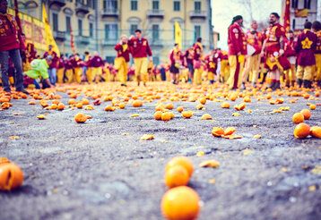 Karneval in Ivrea, Orangenschlacht, sehr viele Orangen liegen auf einem Platz in Ivrea, verkleidete Männer sthen herum