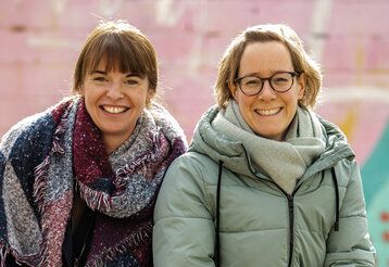 Die Gründerinnen der Initiative Kleeblatt Simone Eßer und Eva Schwientek vor einer Mauer, die rosa und türkis angemalt ist