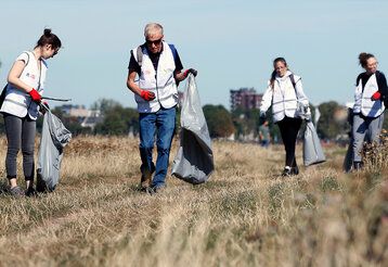 Vier Personen laufen mit Mülltüten auf einer vertrockneten Wiese und sammeln Müll auf