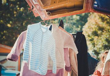 gebrauchte Kinderkleidung hängt an der geöffneten Heckklappe eines Transporters, sonnige Stimmung
