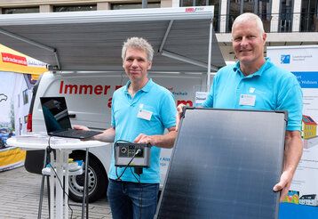Zwei Männer stehen vor dem Klimamobil und präsentieren eine Solarenergieanlage