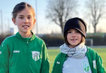 Zwei Mädchen in Fußballtrikots stehen auf einem Fußballplatz