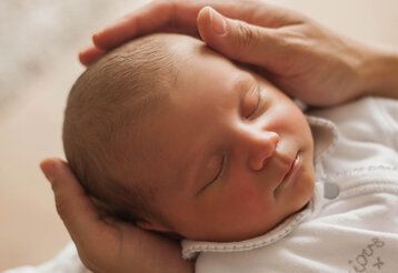 Schlafendes Neugeborenes dessen Kopf in den Händen eines Erwachsenen gehalten wird