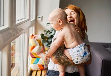 Junge Frau trägt Baby auf dem Arm, das eine Stoffwindel trägt, die Mutter lacht