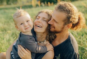 Kleinkind und Eltern auf einer Wiese, sie umarmen sich und lachen entspannt