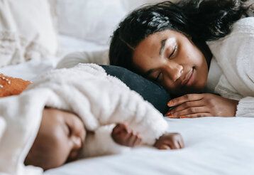 Ein neugeborenes Baby liegt auf einem Bett und schläft, die Mutter schmiegt sich an und schläft auch