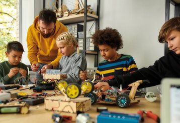 Vier Schüler:innen bauen Roboter, Lehrer hilft