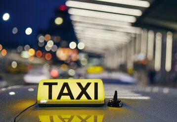 Das Dach eines Taxis mit einem leuchtenden Taxischild, im Hintergund verschwommene Lichter, Stadtszene