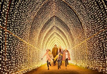 Eine Familie mit drei Kindern in Winterkleidung läuft gemeinsam durch einen mit Licherketten illuminierten Tunnel.