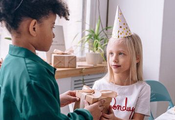 Ein Mädchen mit einem Partyhütchen bekommt von einem anderen Kind ein Geschenk überreicht