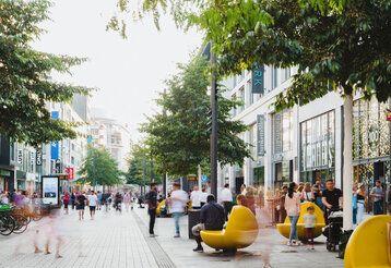 Die belebte Fußgängerzone auf der Schadow Straße im Sommer, gelbe Sitzelemente rechts im Bild