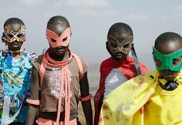 Vier schwarze Jungen laufen mit bunten Sperhelden-Masken und Umhängen  auf die Kamera zu