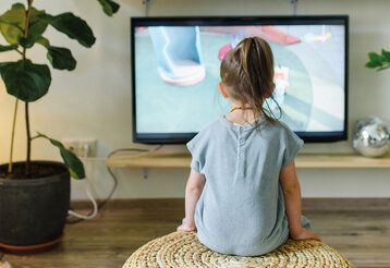 ein kleines Mädchen sitzt vor dem Fernseher, man sieht es von hinten
